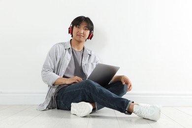 Photo of Student with headphones and laptop studying on floor indoors