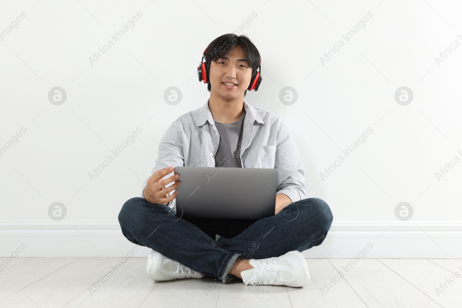Student with headphones and laptop studying on floor indoors Photo of Student with headphones and laptop studying on floor indoors
