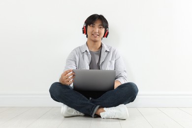 Photo of Student with headphones and laptop studying on floor indoors