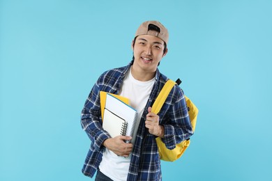 Photo of Student with backpack and notebooks on light blue background