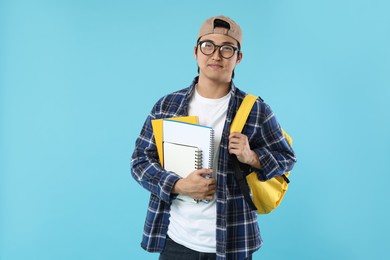Photo of Student with backpack and notebooks on light blue background