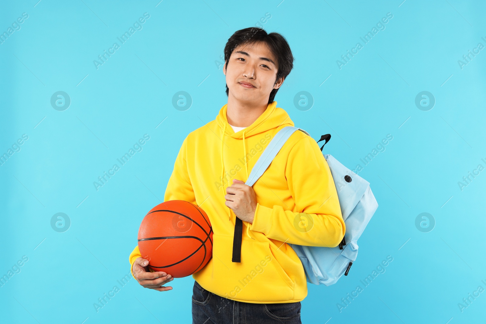 Photo of Student with basketball ball and backpack on light blue background