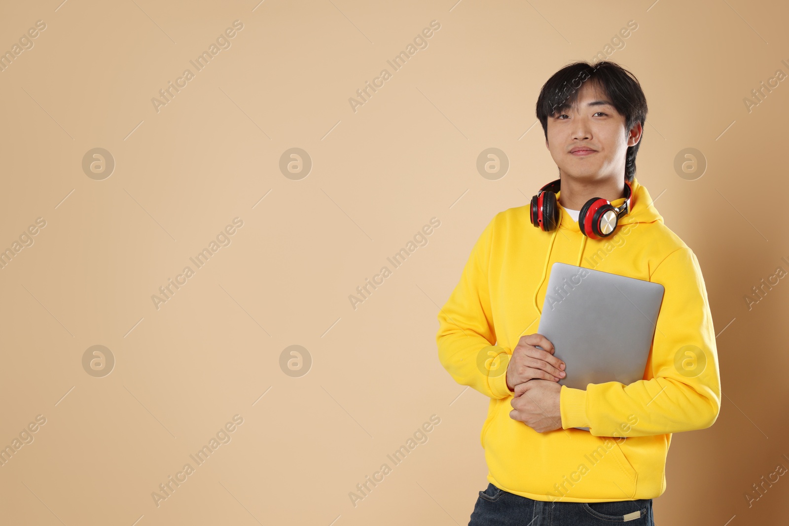 Student with headphones and laptop on beige background, space for text Photo of Student with headphones and laptop on beige background, space for text