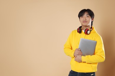 Photo of Student with headphones and laptop on beige background, space for text