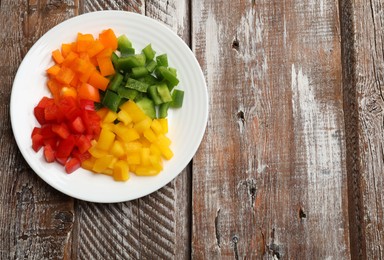 Photo of Cut colorful bell peppers on wooden table, top view. Space for text