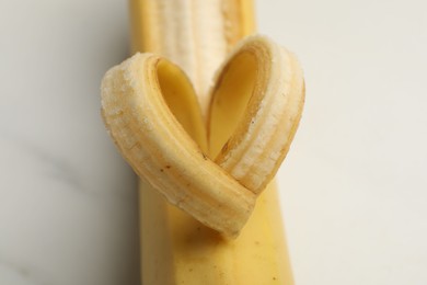 Photo of Banana with heart made of peel on white table, closeup