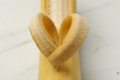 Photo of Banana with heart made of peel on white table, closeup