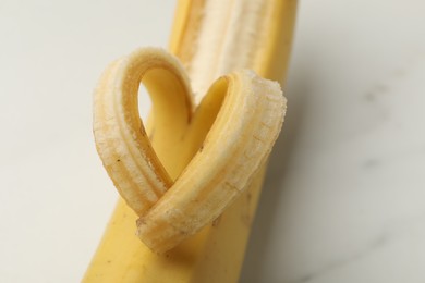 Photo of Banana with heart made of peel on white table, closeup