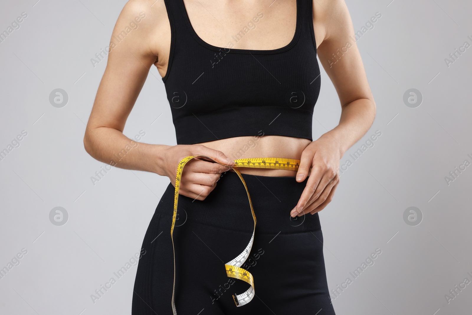 Woman measuring her belly with tape on gray background, closeup Photo of Woman measuring her belly with tape on gray background, closeup