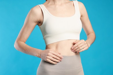 Photo of Beautiful woman with flat belly on light blue background, closeup