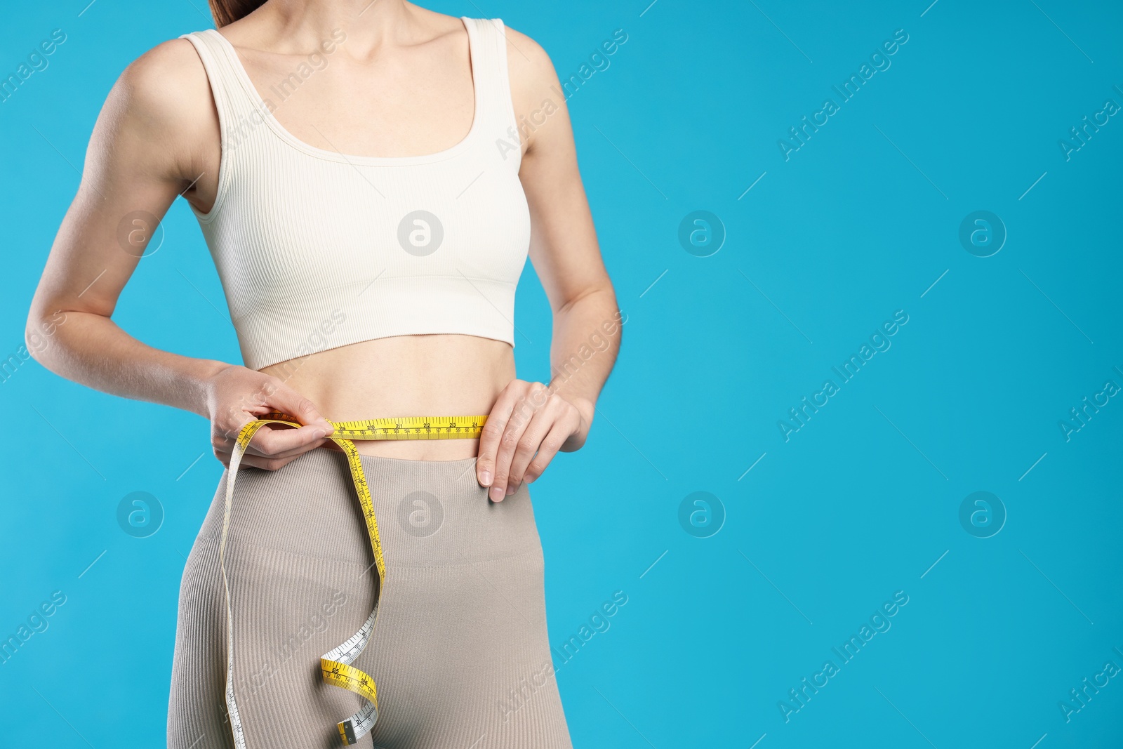 Woman measuring her belly with tape on light blue background, closeup. Space for text Photo of Woman measuring her belly with tape on light blue background, closeup. Space for text