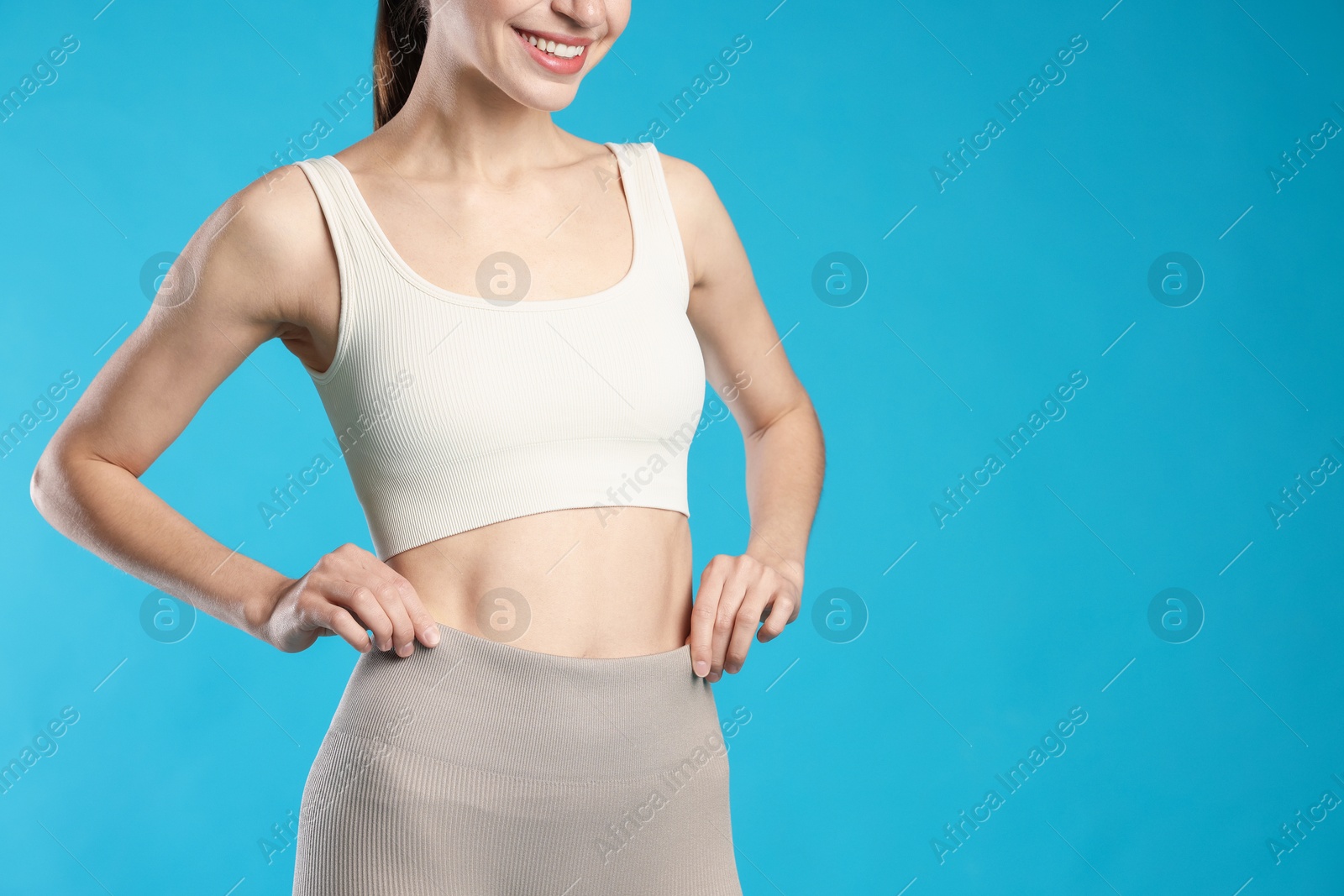 Beautiful woman with flat belly on light blue background, closeup. Space for text Photo of Beautiful woman with flat belly on light blue background, closeup. Space for text