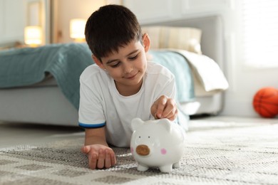 Photo of Boy putting pocket money into piggybank at home