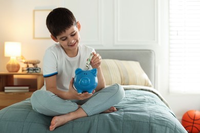 Photo of Boy putting pocket money into piggybank on bed at home. Space for text