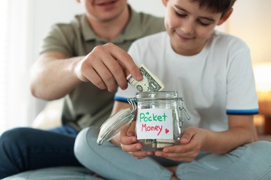 Photo of Father and son putting pocket money into jar on bed at home, selective focus