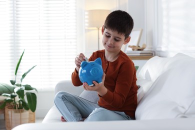 Photo of Boy putting his pocket money into piggybank on sofa at home