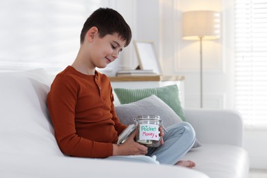 Photo of Boy with jar of pocket money on sofa at home