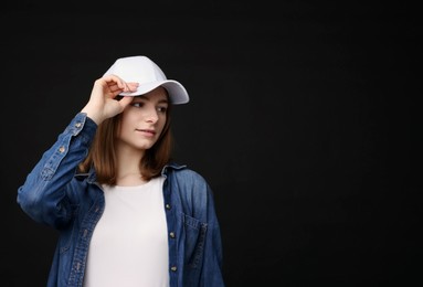 Photo of Young woman wearing stylish white baseball hat on black background, space for text