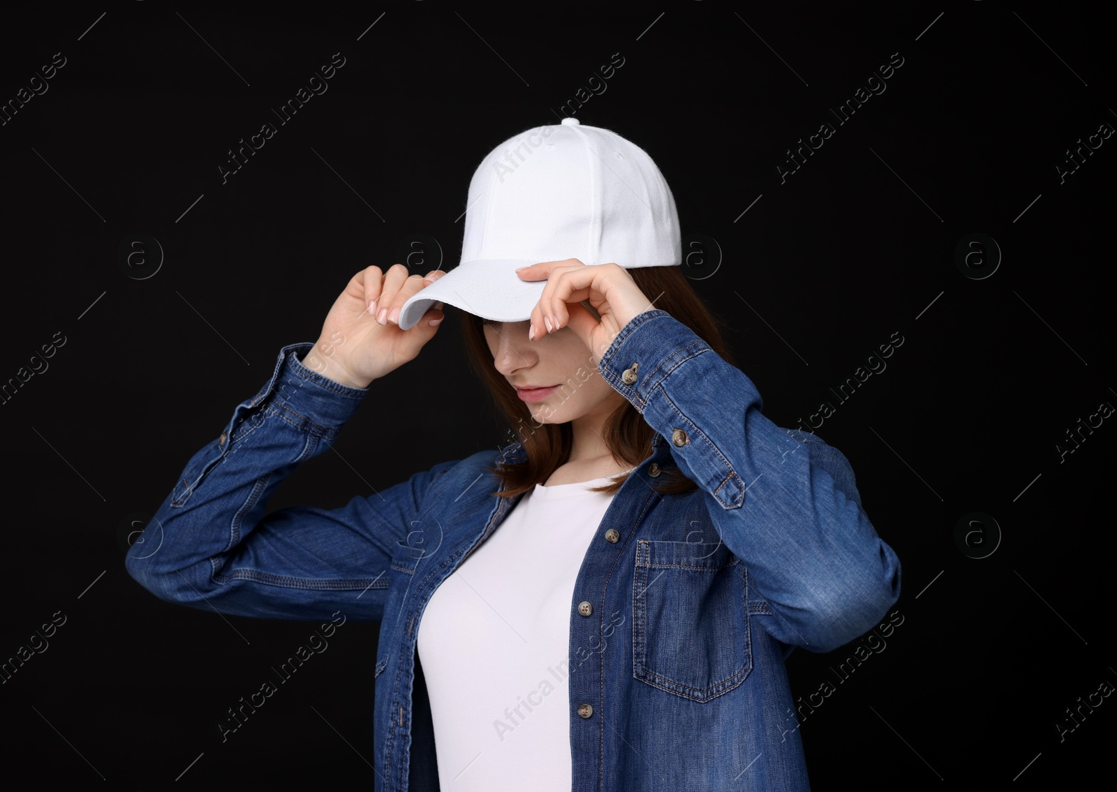 Young woman wearing stylish white baseball hat on black background Photo of Young woman wearing stylish white baseball hat on black background