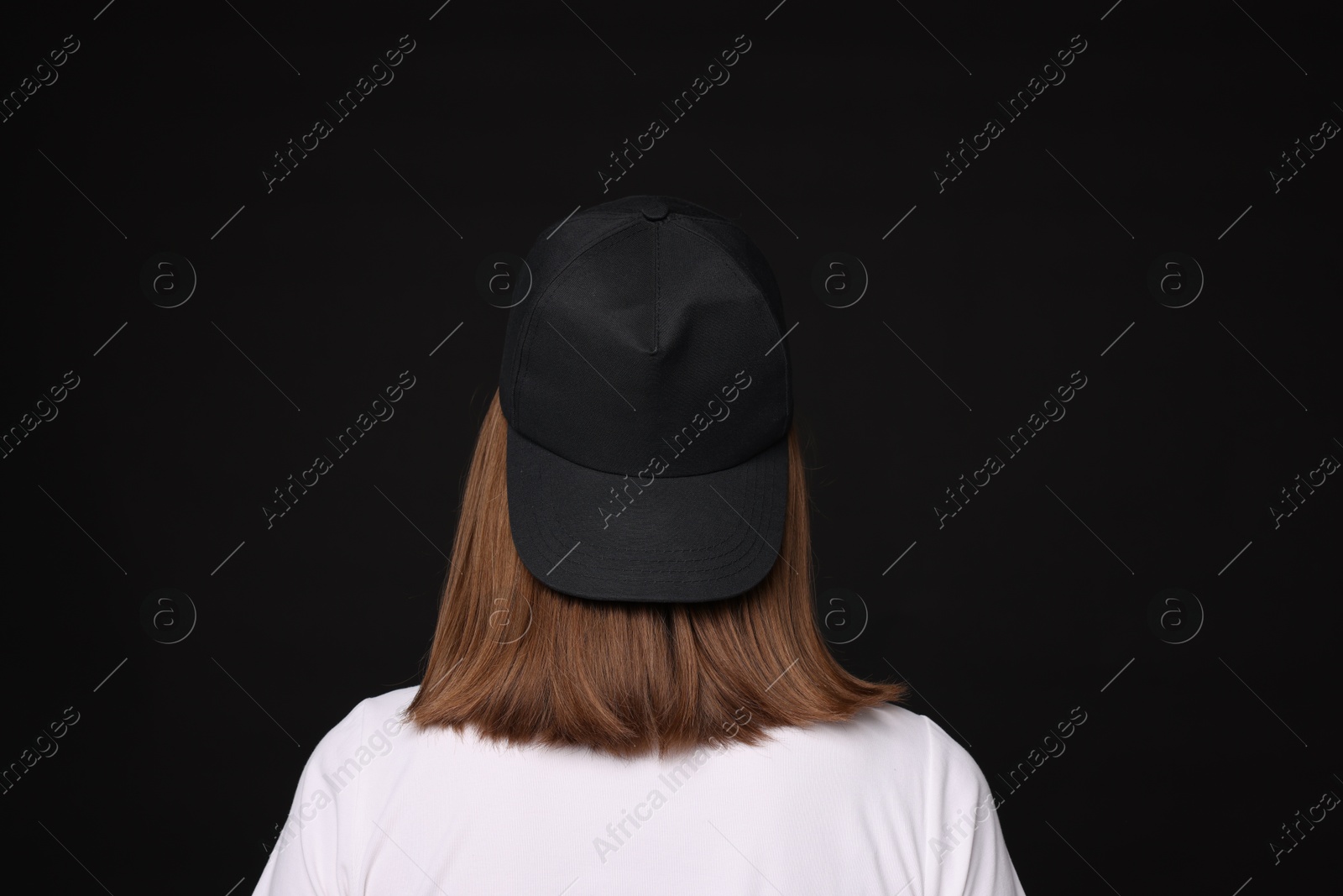 Young woman wearing stylish baseball hat on black background, back view Photo of Young woman wearing stylish baseball hat on black background, back view