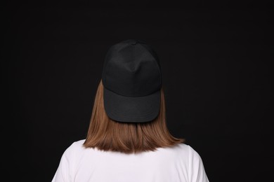 Photo of Young woman wearing stylish baseball hat on black background, back view