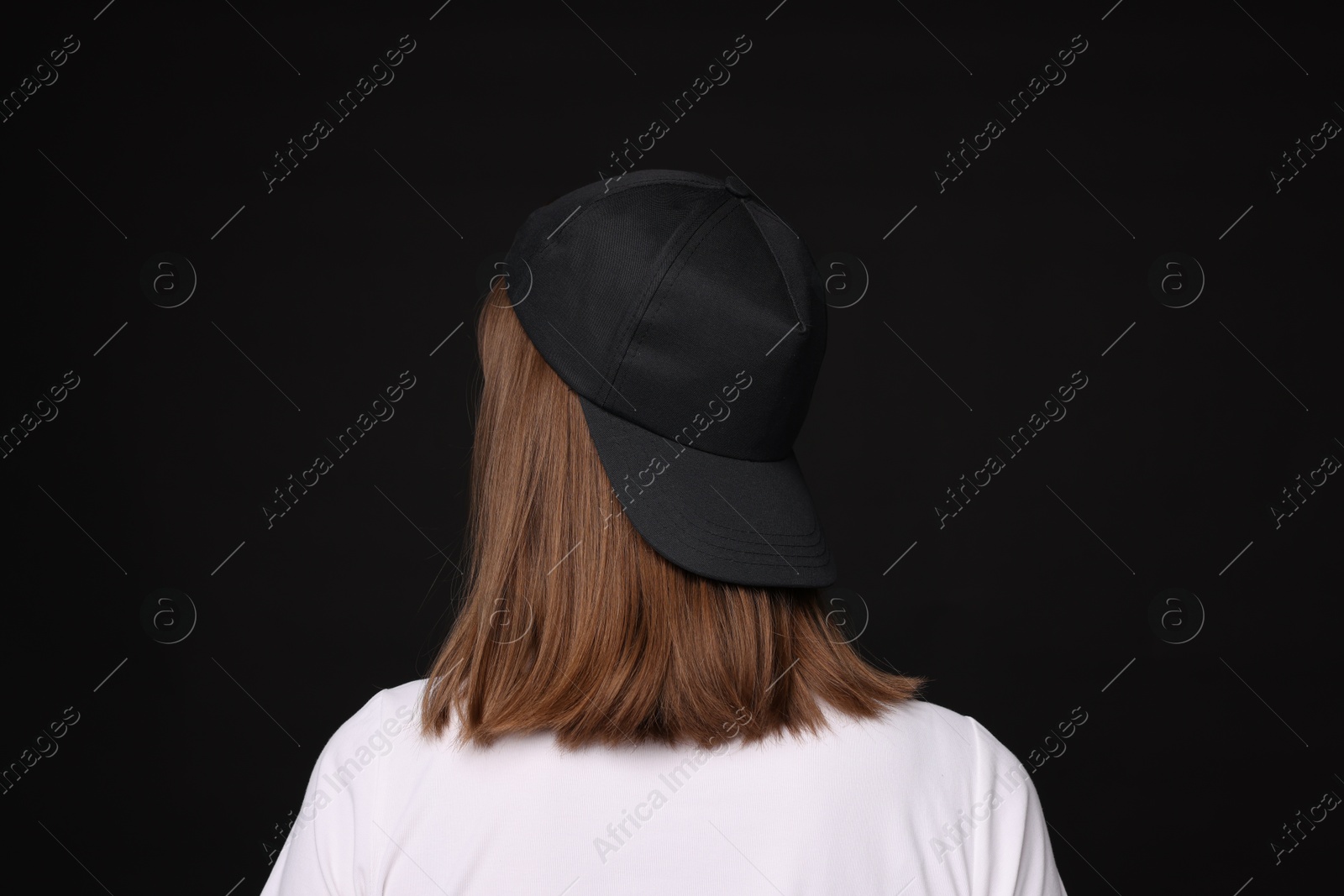Young woman wearing stylish baseball hat on black background, back view Photo of Young woman wearing stylish baseball hat on black background, back view