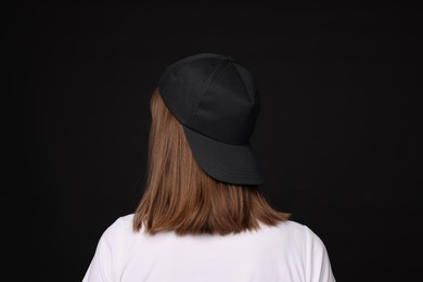 Photo of Young woman wearing stylish baseball hat on black background, back view