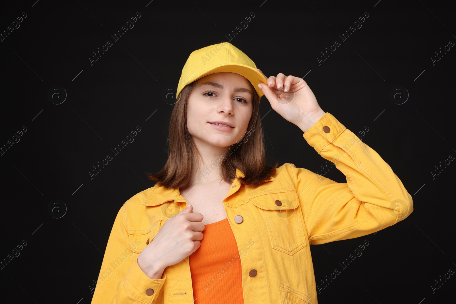 Photo of Young woman wearing stylish yellow baseball hat on black background