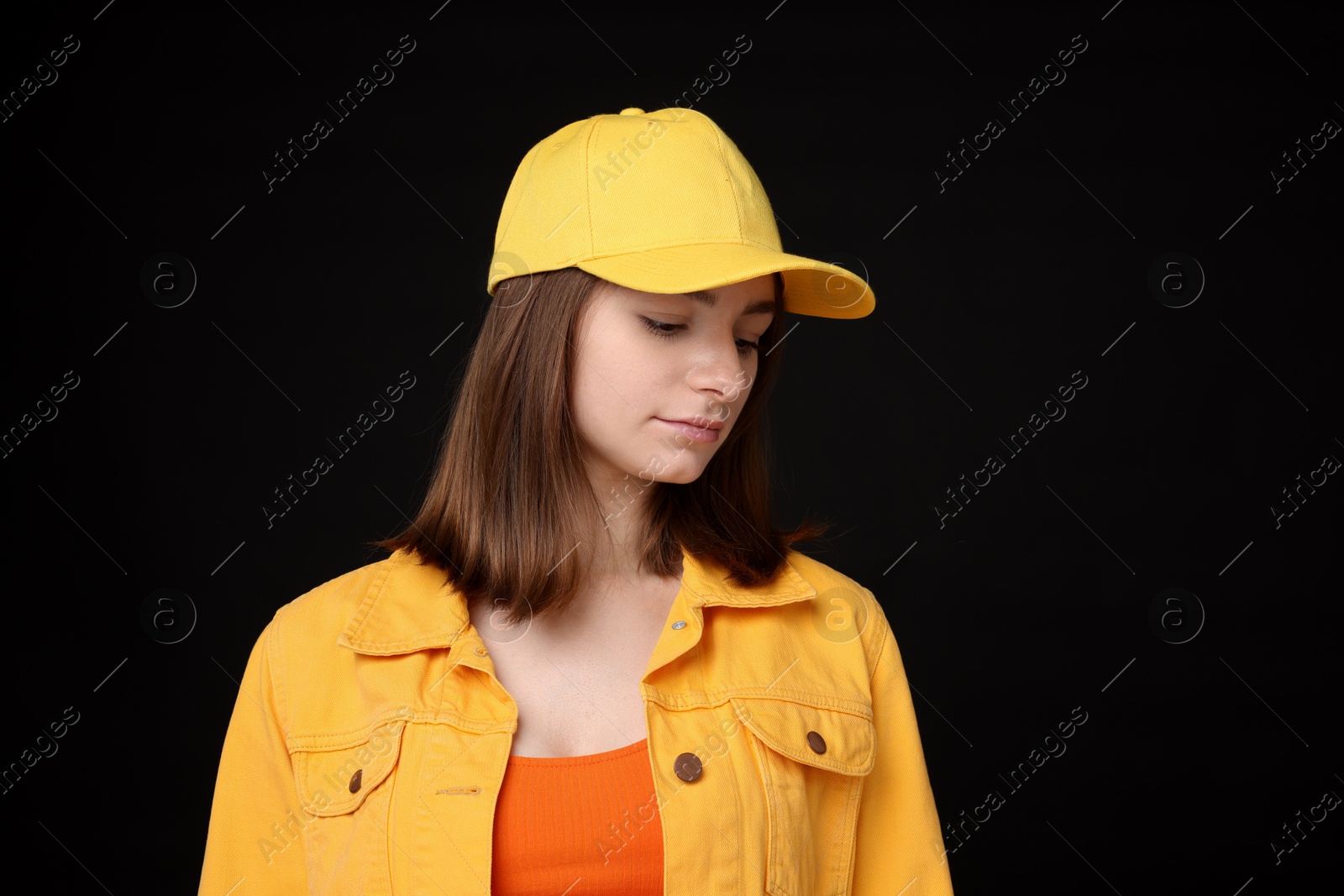 Photo of Young woman wearing stylish yellow baseball hat on black background
