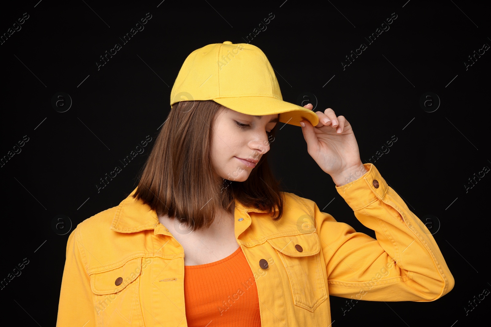 Photo of Young woman wearing stylish yellow baseball hat on black background