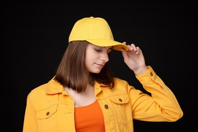 Photo of Young woman wearing stylish yellow baseball hat on black background