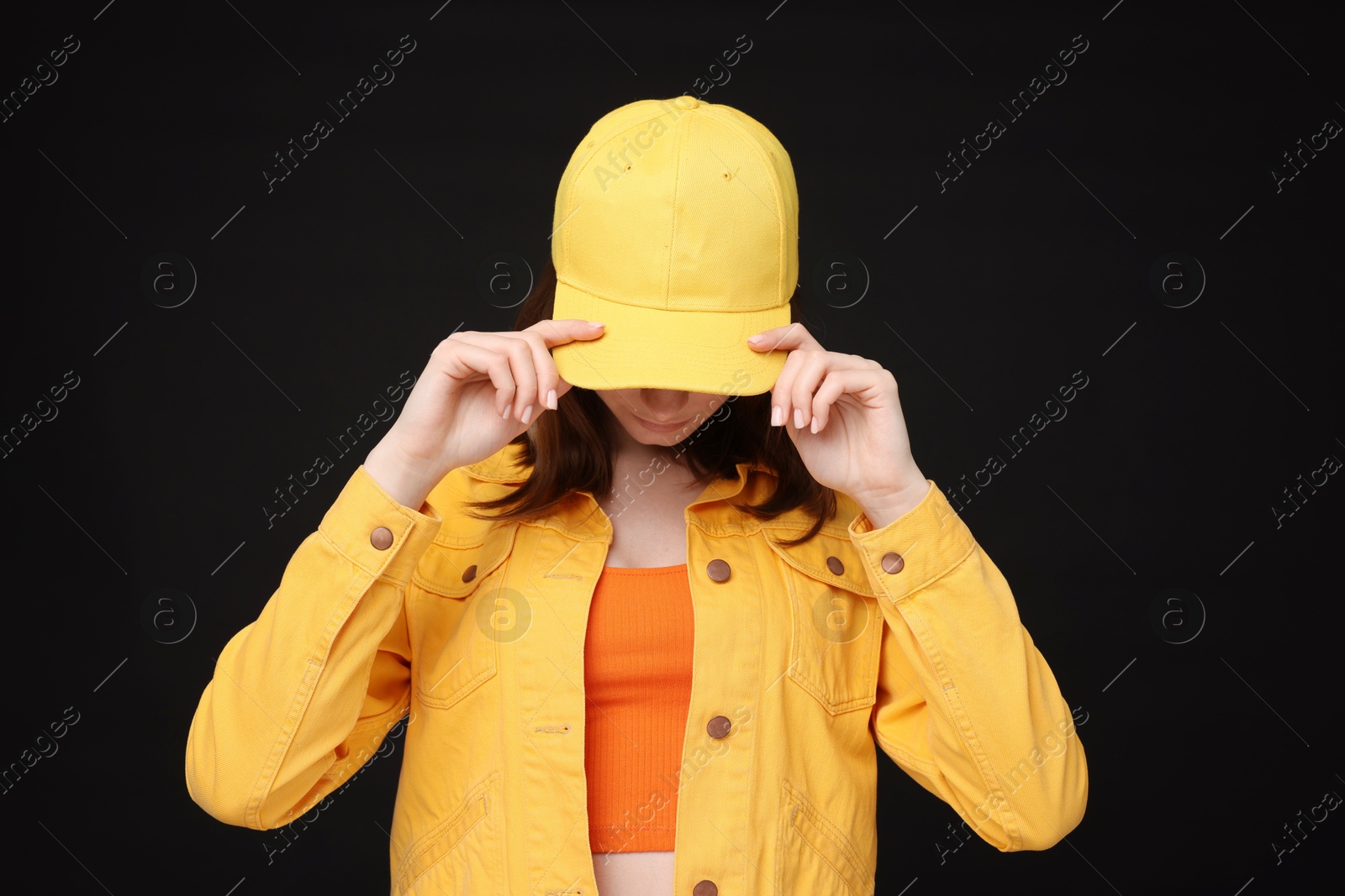 Photo of Young woman wearing stylish yellow baseball hat on black background