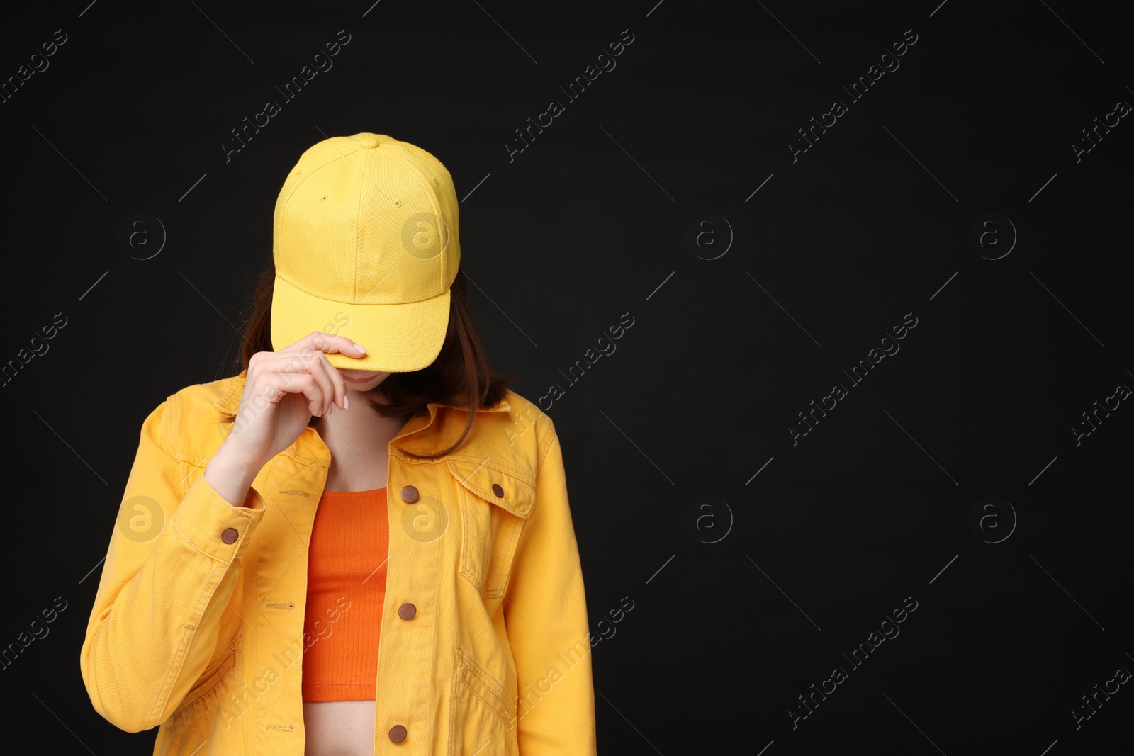 Photo of Young woman wearing stylish yellow baseball hat on black background, space for text