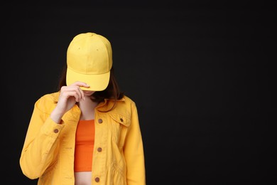 Photo of Young woman wearing stylish yellow baseball hat on black background, space for text