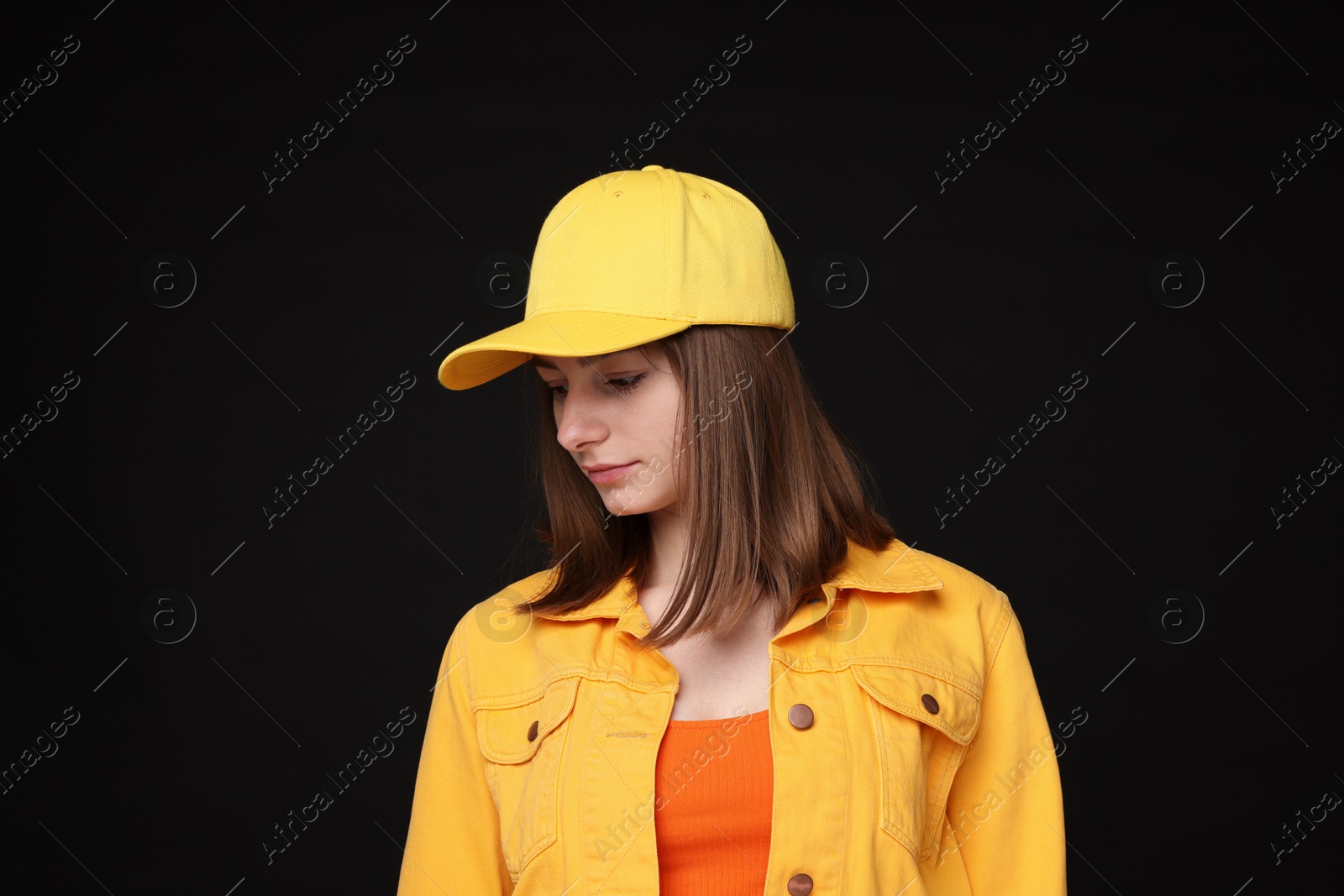 Photo of Young woman wearing stylish yellow baseball hat on black background
