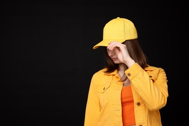 Photo of Young woman wearing stylish yellow baseball hat on black background, space for text