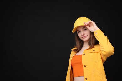 Photo of Young woman wearing stylish yellow baseball hat on black background, space for text