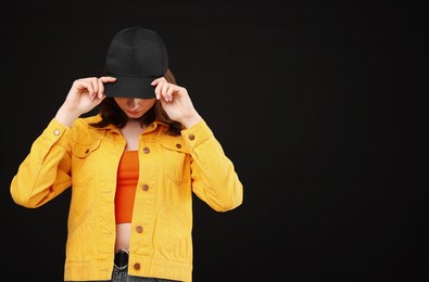 Photo of Young woman wearing stylish baseball hat on black background, space for text