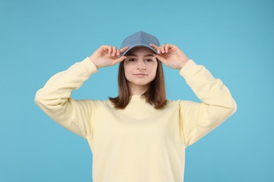Photo of Young woman wearing stylish denim baseball hat on light blue background