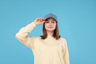 Photo of Young woman wearing stylish denim baseball hat on light blue background