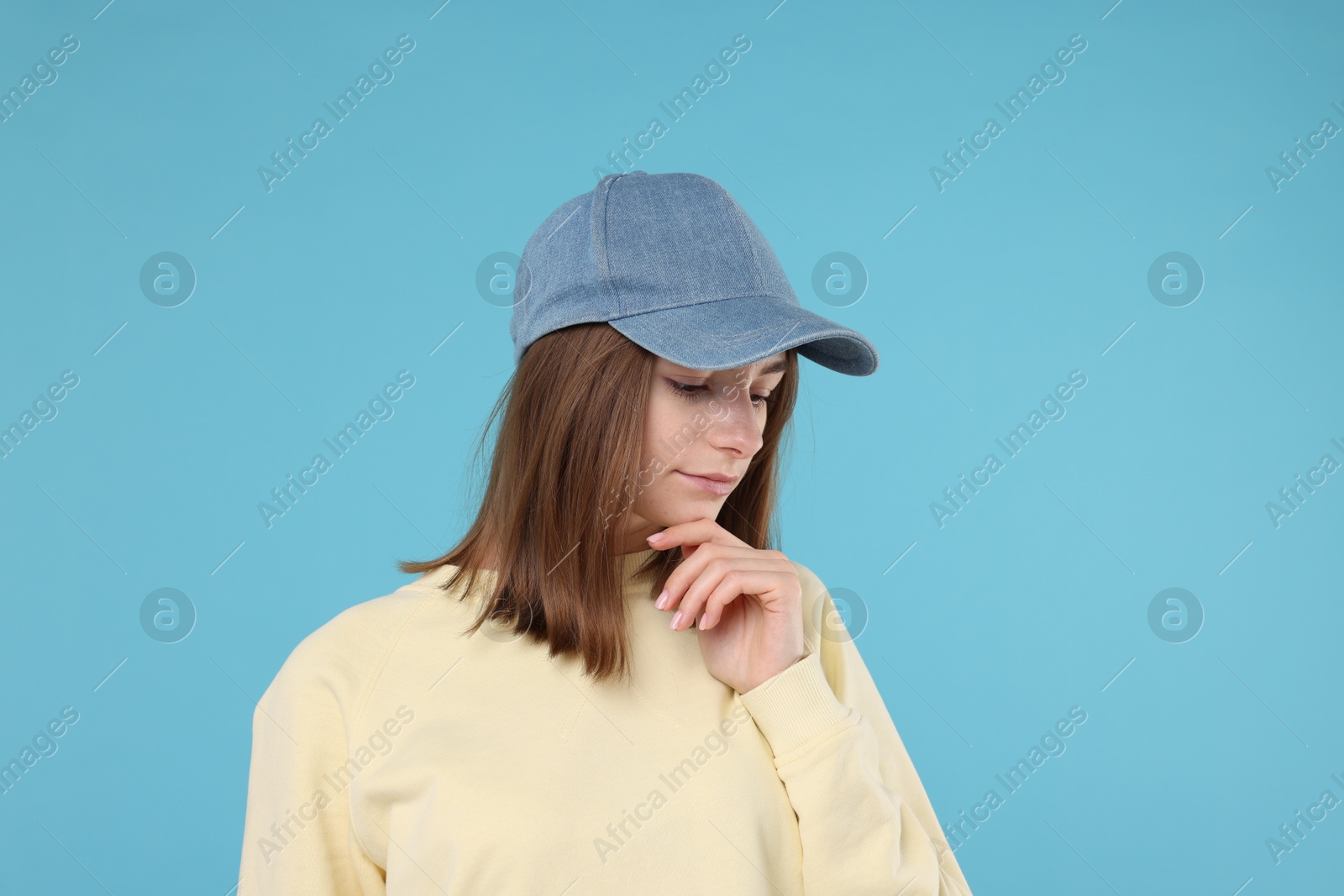 Photo of Young woman wearing stylish denim baseball hat on light blue background