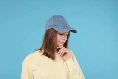 Photo of Young woman wearing stylish denim baseball hat on light blue background