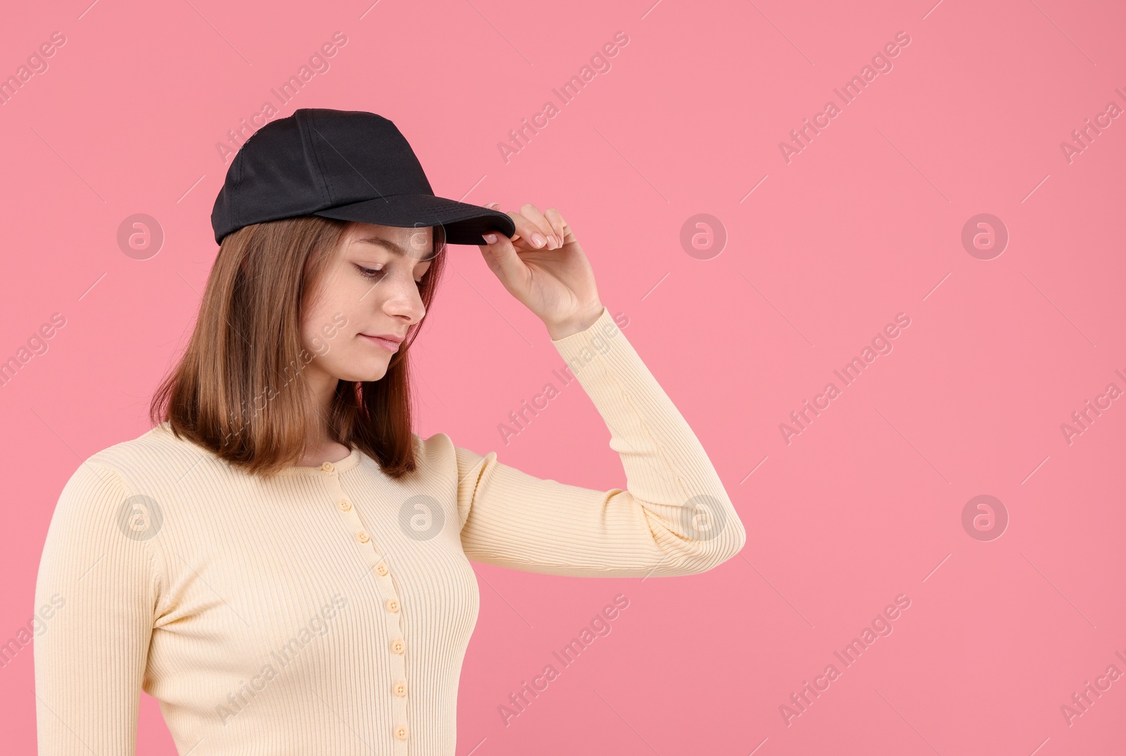 Photo of Young woman wearing stylish black baseball hat on pink background, space for text
