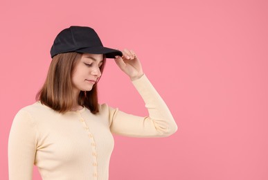 Photo of Young woman wearing stylish black baseball hat on pink background, space for text