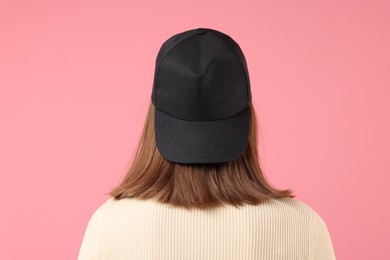 Photo of Young woman wearing stylish black baseball hat on pink background, back view