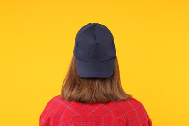 Photo of Young woman wearing stylish black baseball hat on yellow background, back view