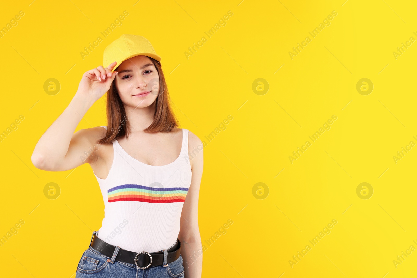 Photo of Young woman wearing stylish baseball hat on yellow background, space for text