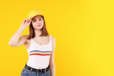 Photo of Young woman wearing stylish baseball hat on yellow background, space for text