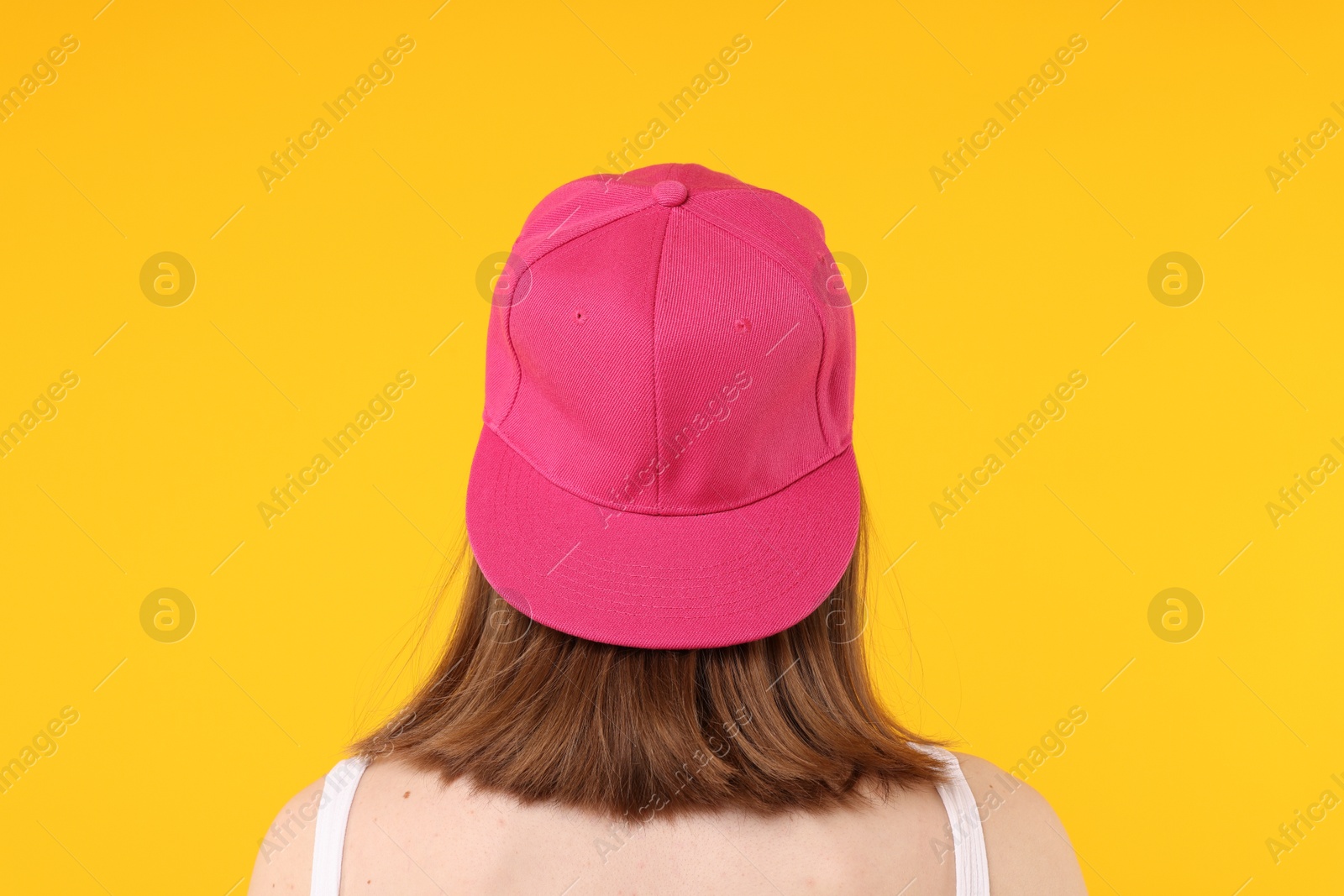 Photo of Young woman wearing stylish pink baseball hat on yellow background, back view