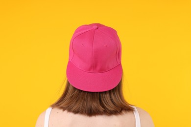 Photo of Young woman wearing stylish pink baseball hat on yellow background, back view
